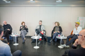 Five panelists sit at the front of an audience.