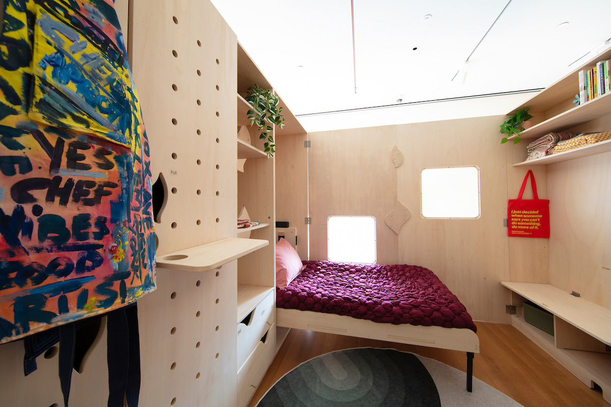 An interior of a bedroom with pale wood walls, a Murphy bed, and build-in shelving.
