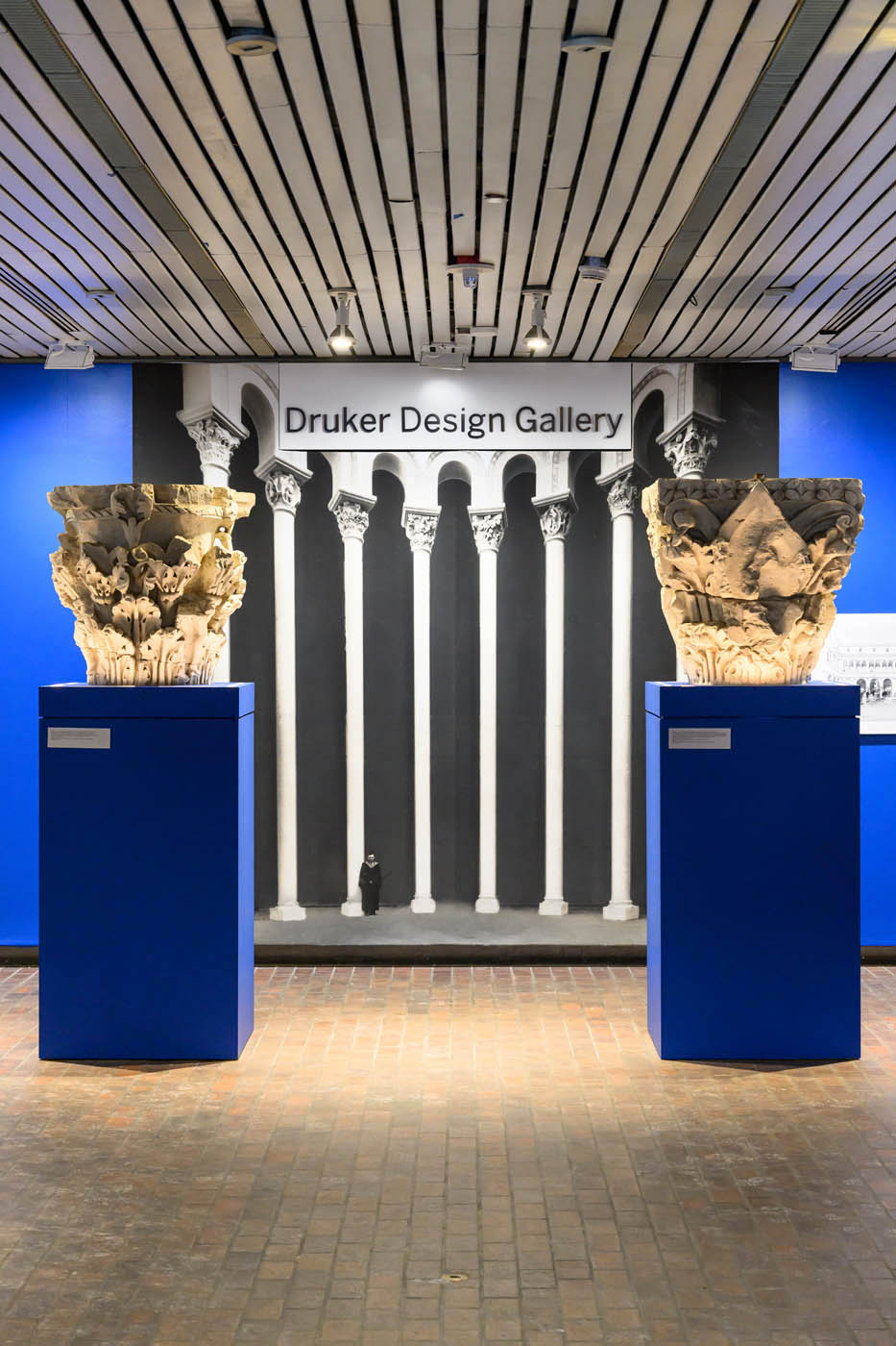 Two plaster casts of column capitals on pedestals infront of a mural of columns.