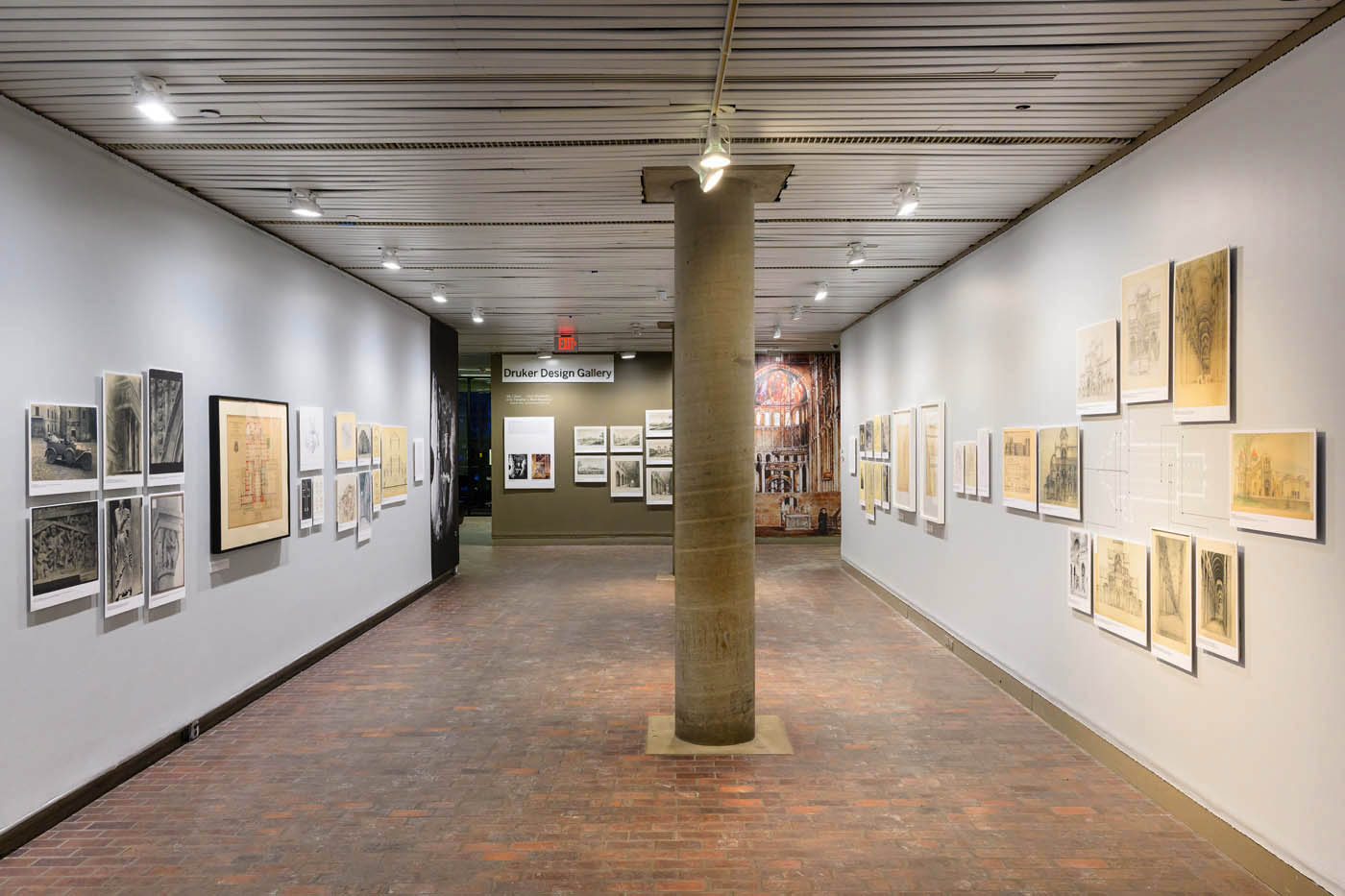 A long view down a narrow gallery. of images displayed on walls. At the end of the hall is a wall of images and a mural depicting a painting of the interior of a church.