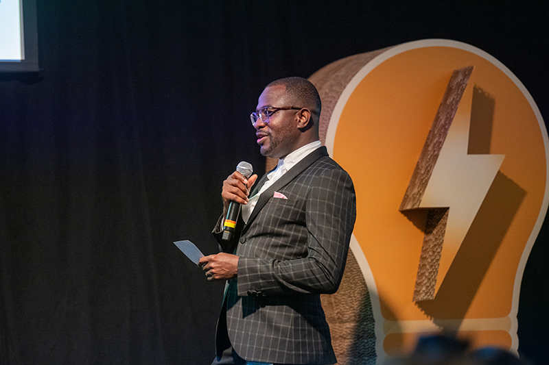Mac Sarbah speaking at a conference with a microphone in hand.