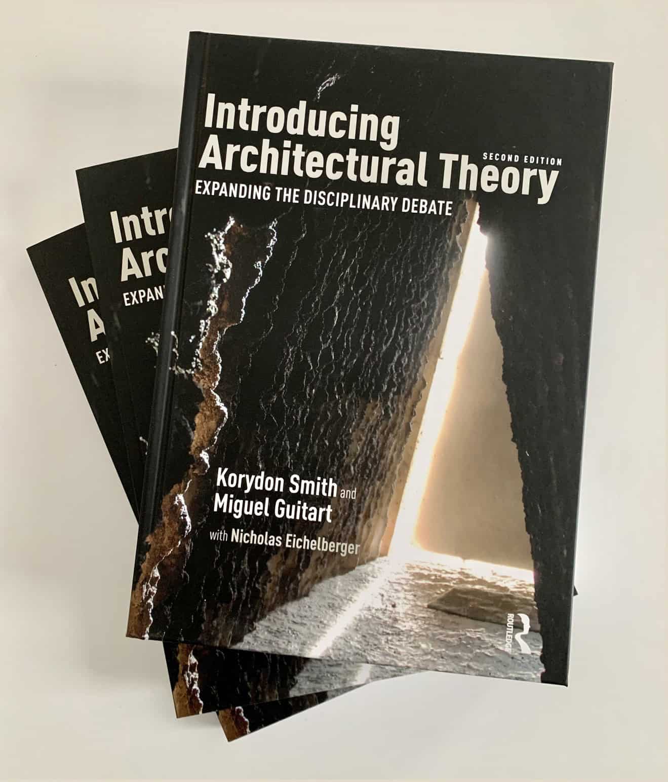 Stack of books for Introducing Architectural Theory. The cover appears to show a cave with light shining in.