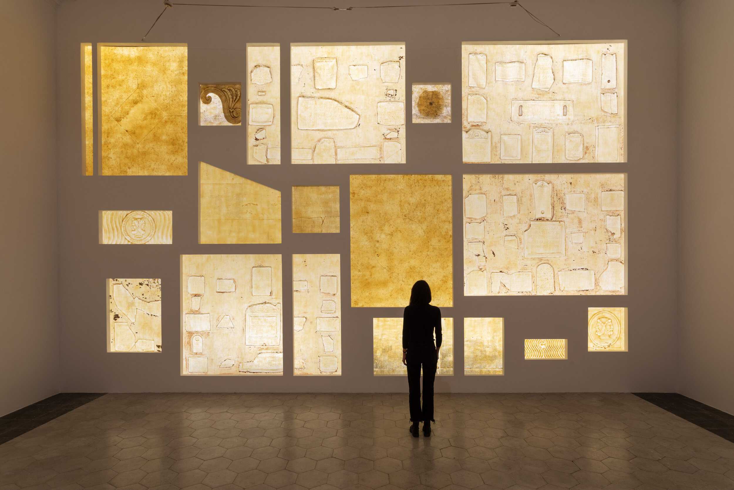 Photograph of woman standing in gallery looking at yellow tinted images.