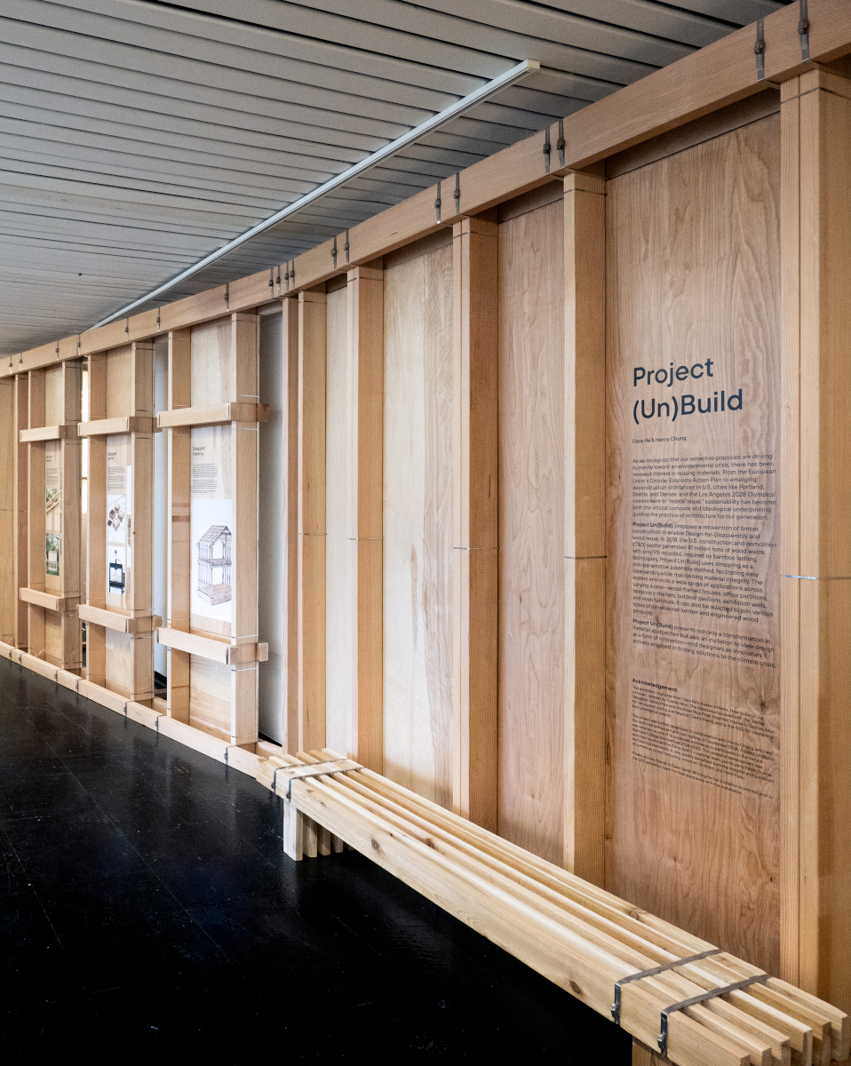A view of the exhibit showing a seating bench in front of a temporary wooden wall with framing studs exposed, all assembled with long steel straps.