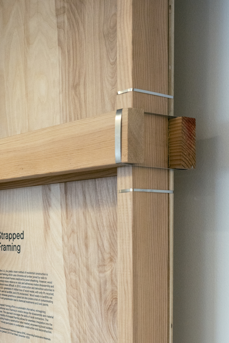 Detail of the exhibit showing a right-angle join of wooden framing studs and cross pieces joined with steel straps.