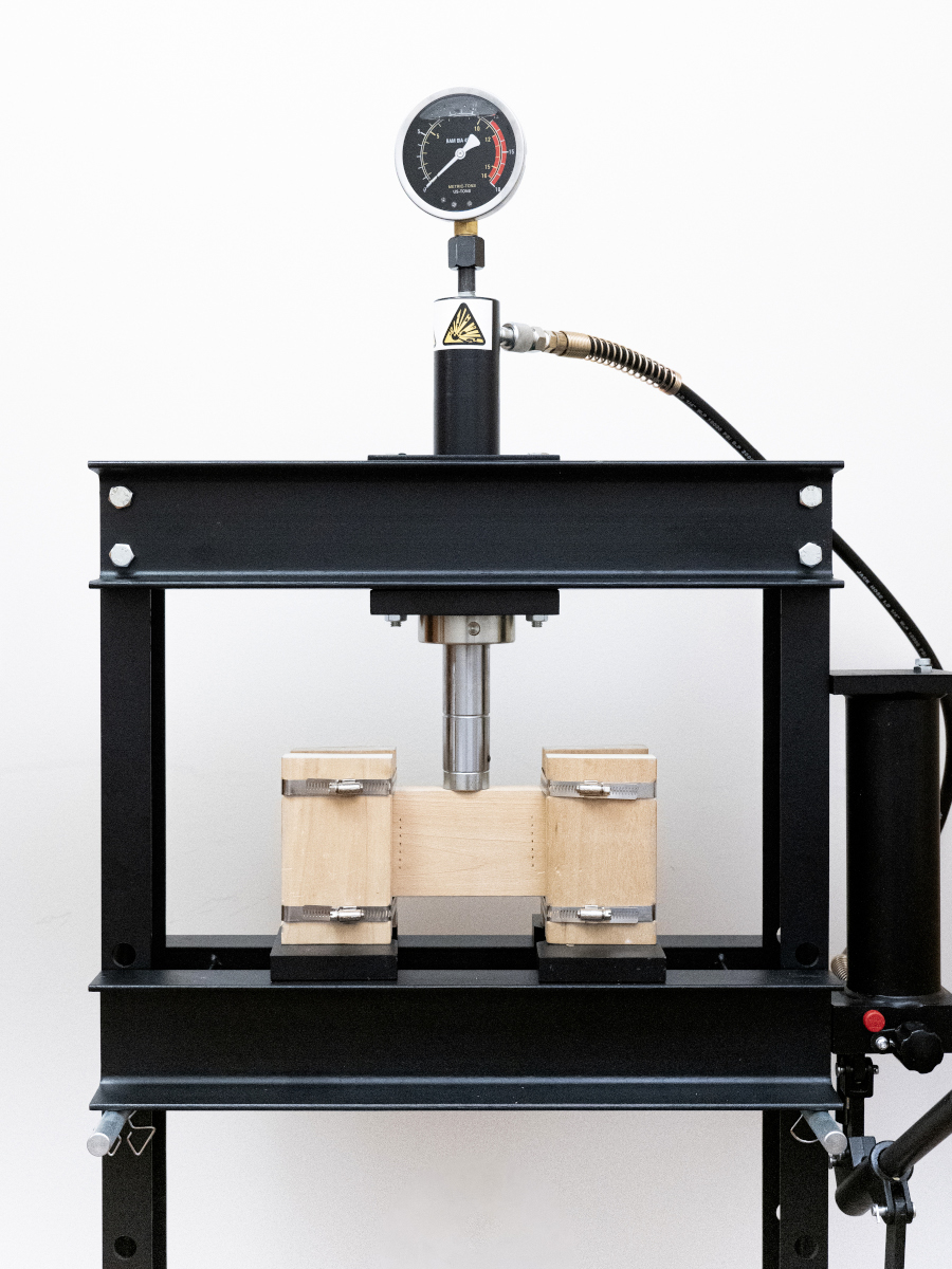 Blocks of wood joined with steel straps being stress-tested in a mechanical press.