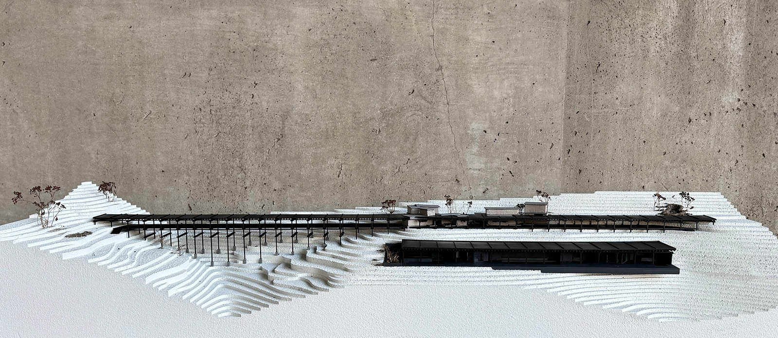 Model of a long brown building on top of rice terraced landscape made from styrofoam