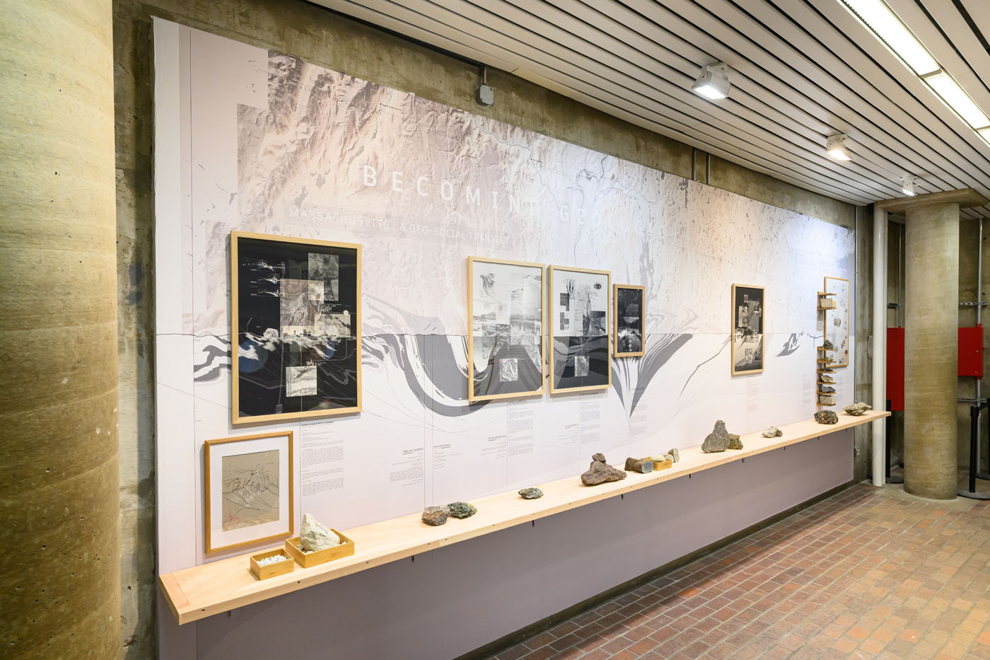 Framed drawings against a wall sized mural of a geologic section of massachusetts. With a shelf in front with rock on top.