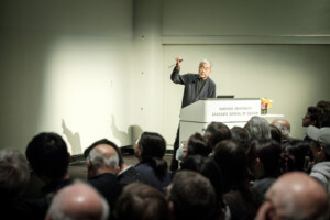 man speaking at podium to crowded auditorium