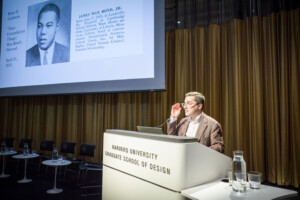 Brian Goldstein stands at the Harvard GSD Lectern. On the screen is an image of Max Bond.