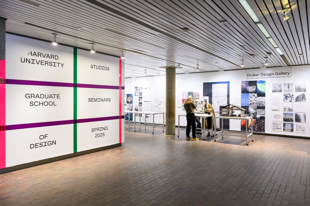 View of the exhibit in Druker Design Gallery showing a variety of images and colorful graphics on the walls and people looking at architectural models on tables.