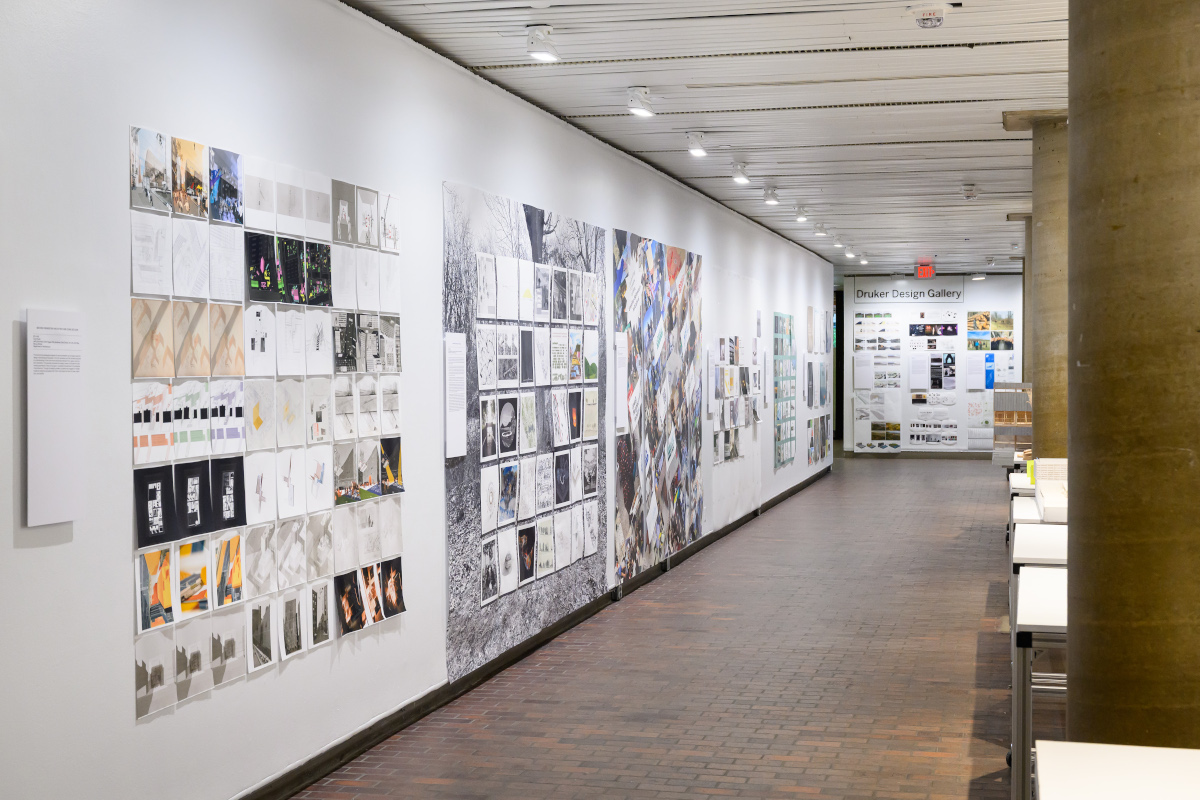 A view of the exhibit in Druker Design Gallery showing walls with a variety of 2D images displayed along it.