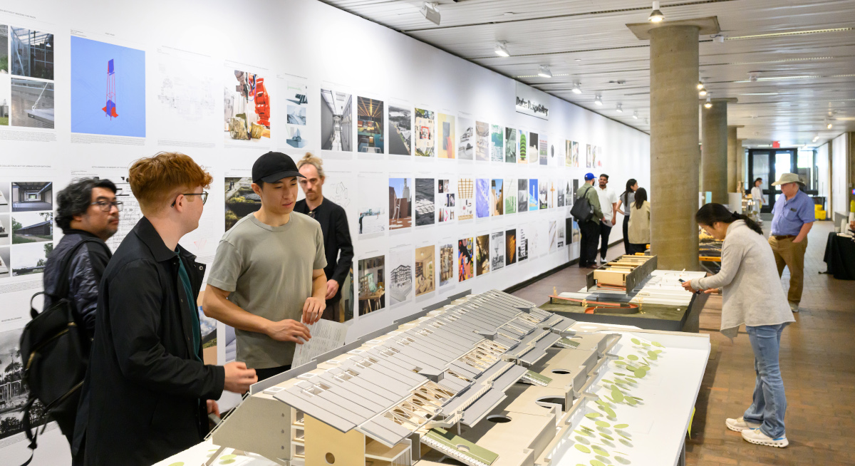 A view of the exhibit in Druker Design Gallery, showing groups of people viewing large architectural models and a wall with a variety of images.