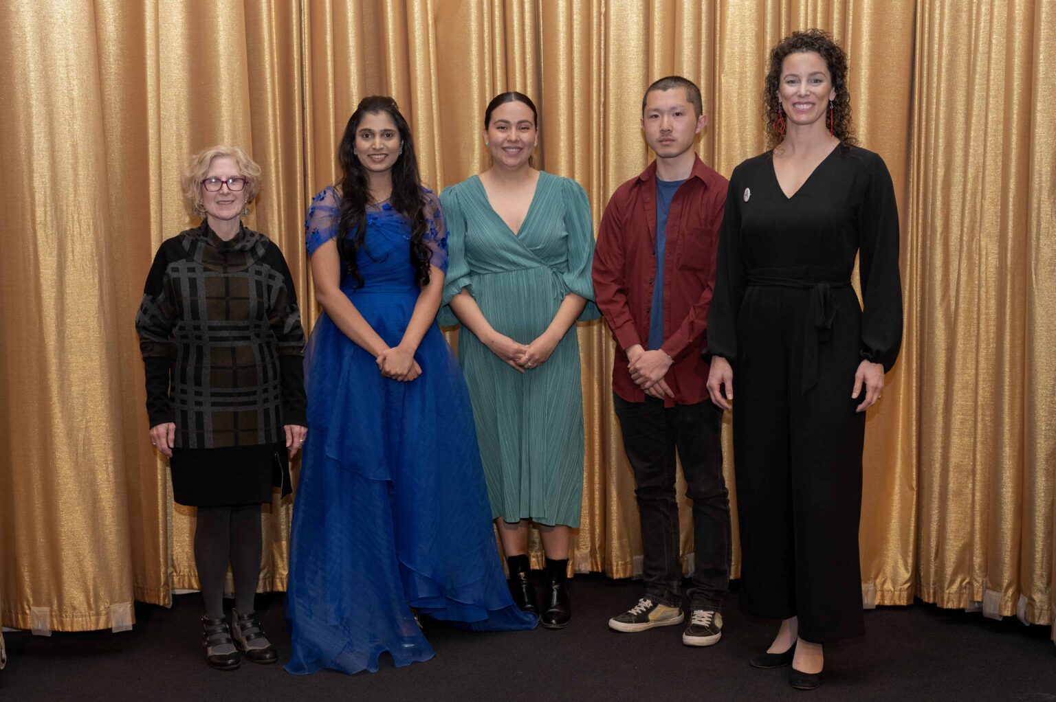 The three student winners along stand in front of gold curtain with a staff member and Alumni Council member.
