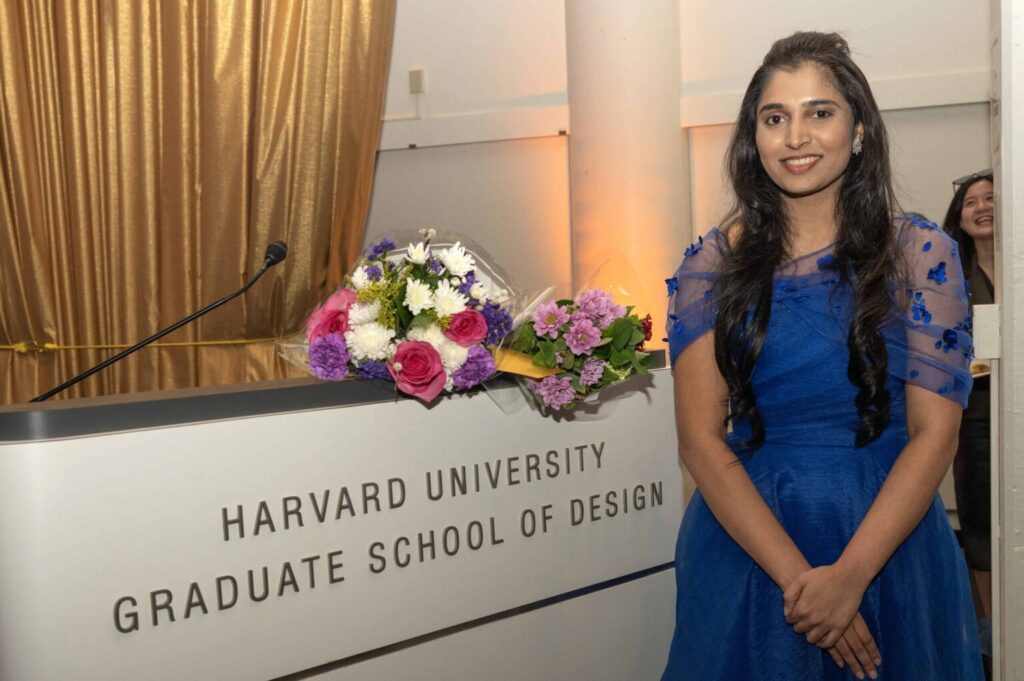 Navya Raju stands beside a Harvard GSD podium and flower bouquet