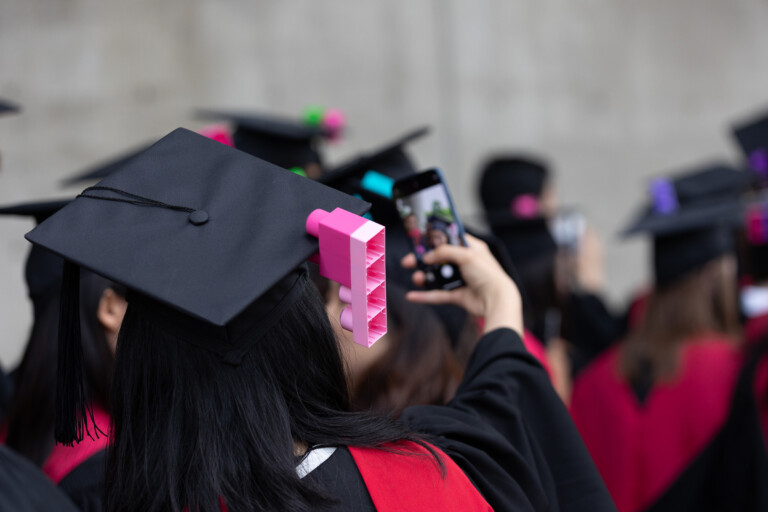 A graduate poses for a selfie with a large lego affixed to their regalia.