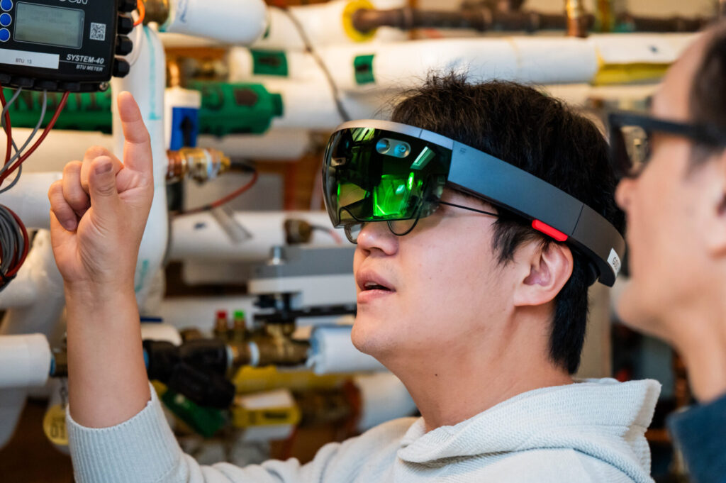 A man looks through VR glasses while a professor looks on.