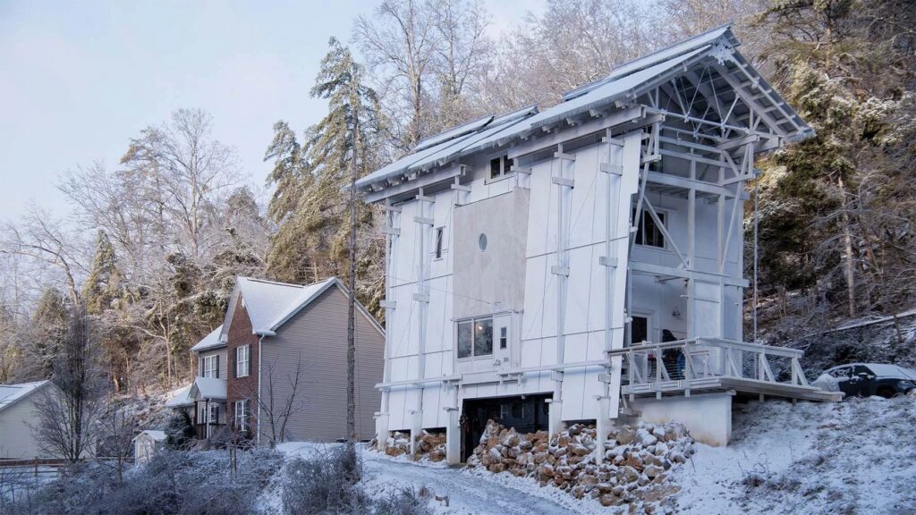 A white home with a visible exoskeleton surrounded by snowy trees
