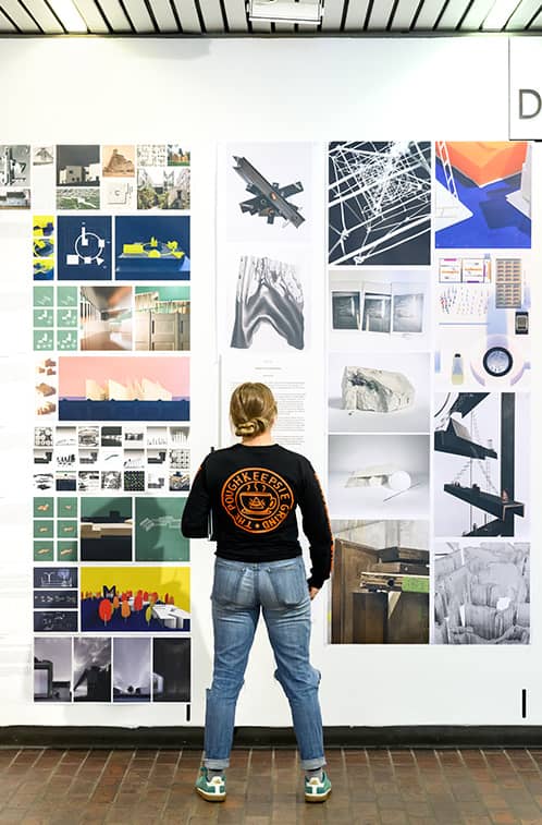 Spring exhibition wall with a student observing the projects.