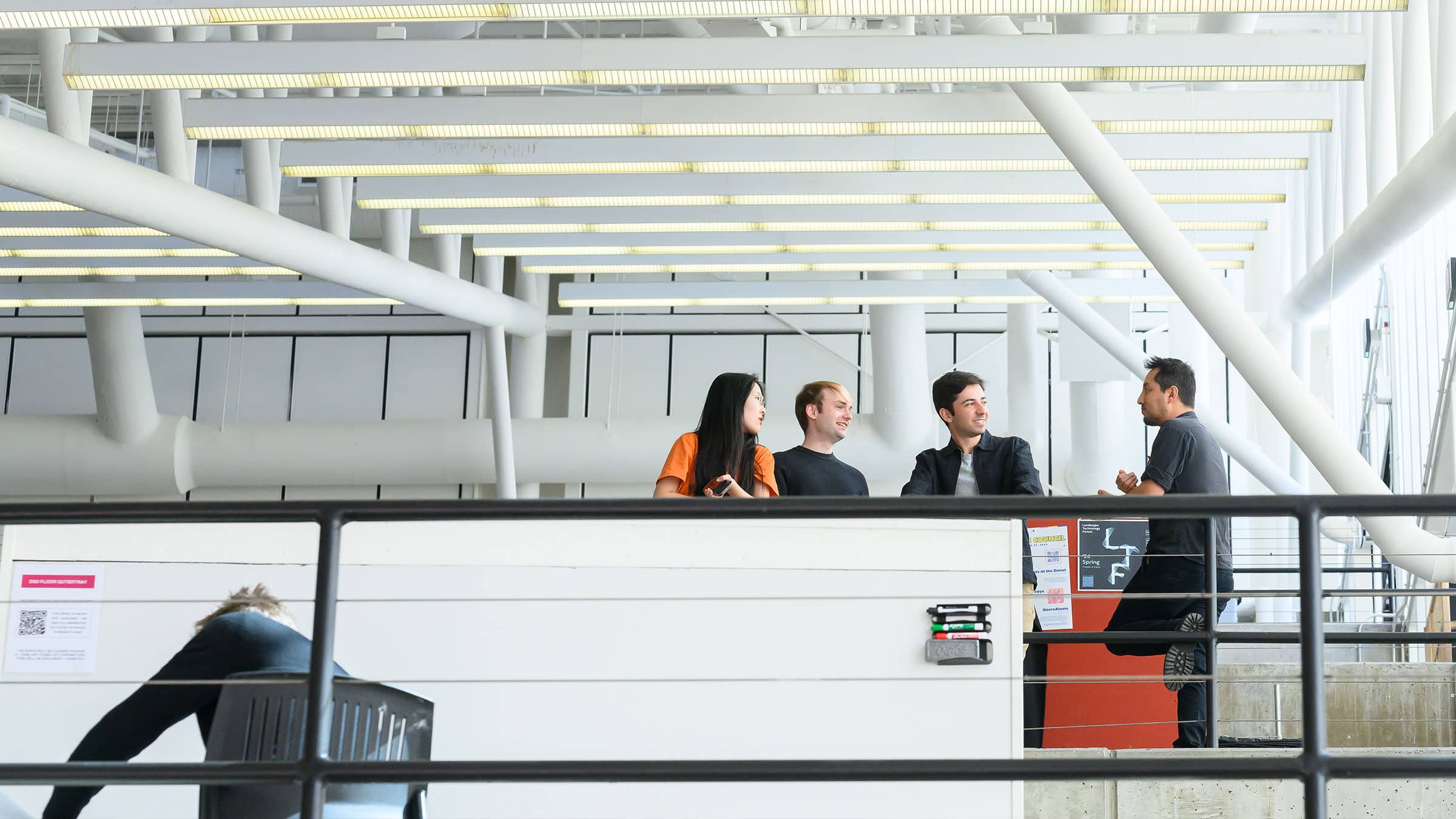 Interior view of a building emphasizing the architecture of the ceiling with a group talking on the landing.
