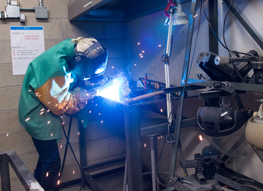 Student in a welding mask cutting metal in a shower of sparks.