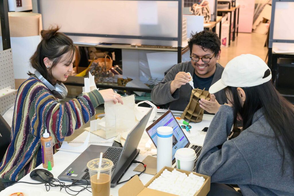 Three students working in the trays with models and laptops