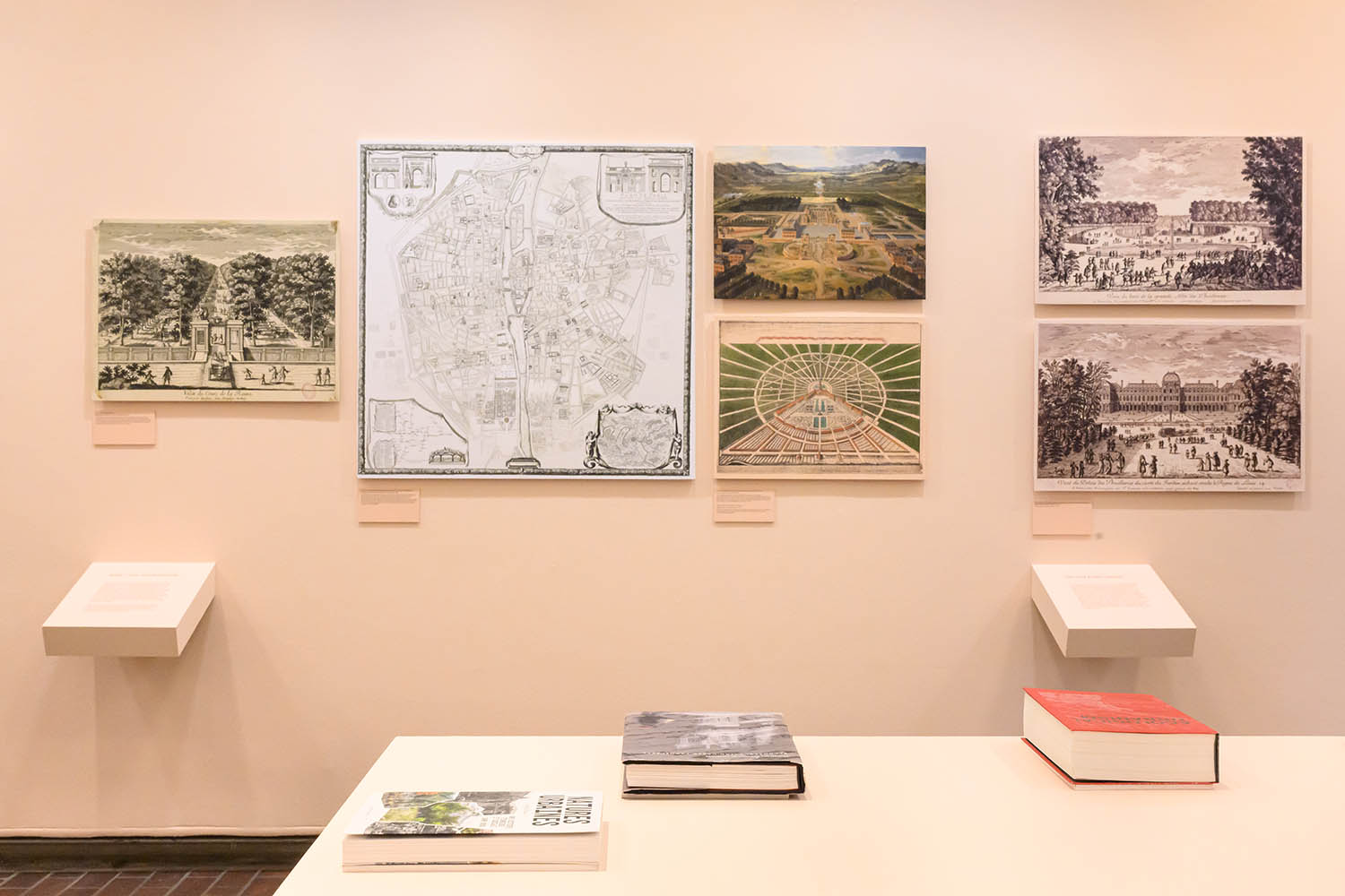 A table of books related to the exhibition infront a of display of 17th century France imagery of urban parks.