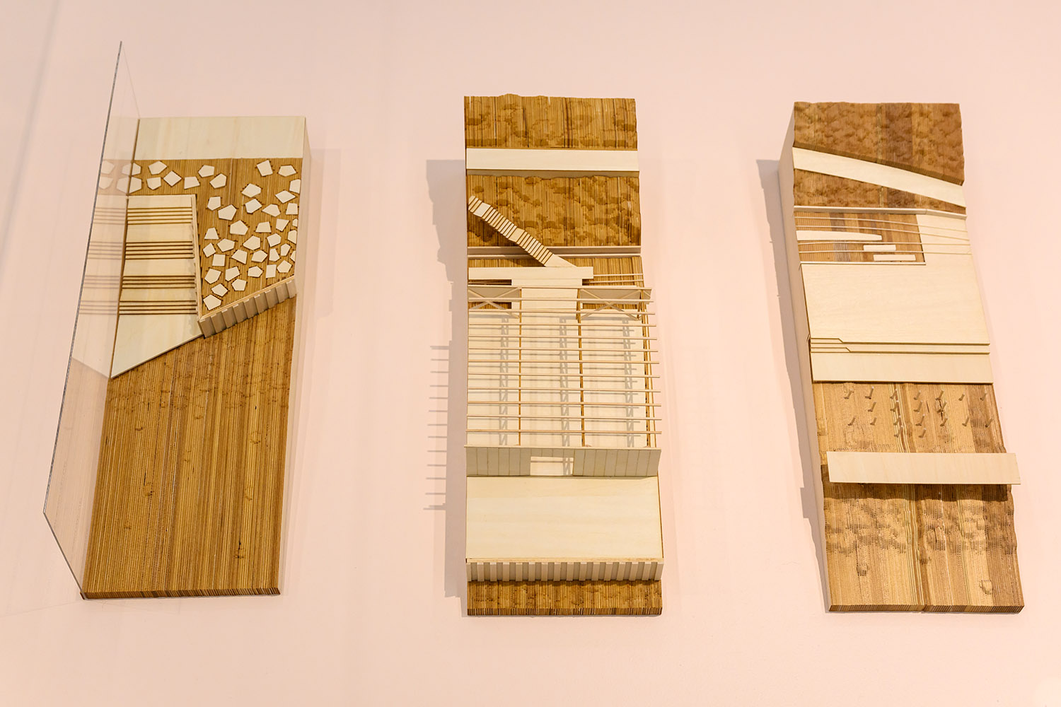 Three wooden architectural models depicting slices of buildings and their landscapes.
