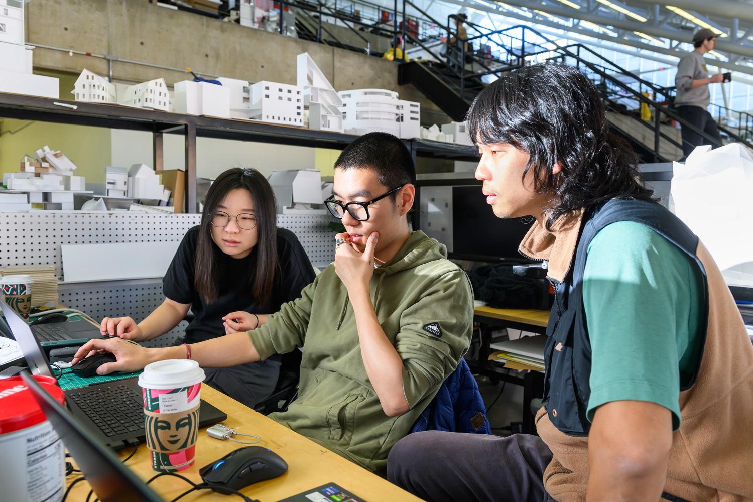 Three students sitting at a desk in the Trays, working at a laptop computer