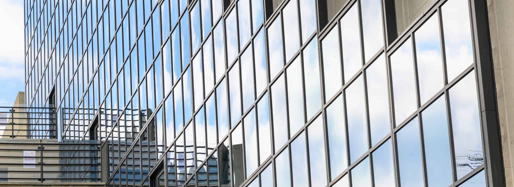 A wall of exterior windows on Gund Hall reflect a blue sky and balconies.