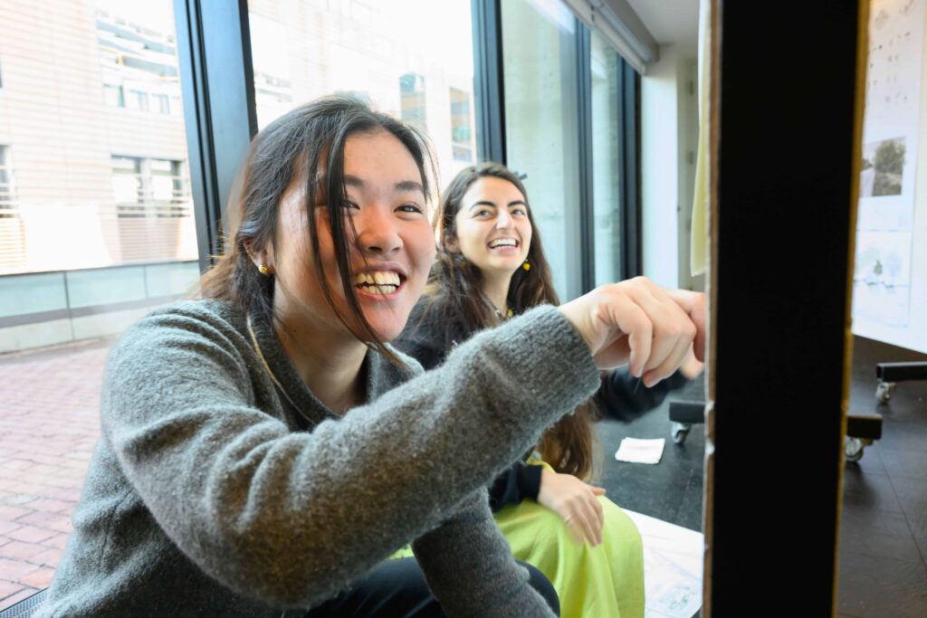 Two students smile as they pin their work to a board