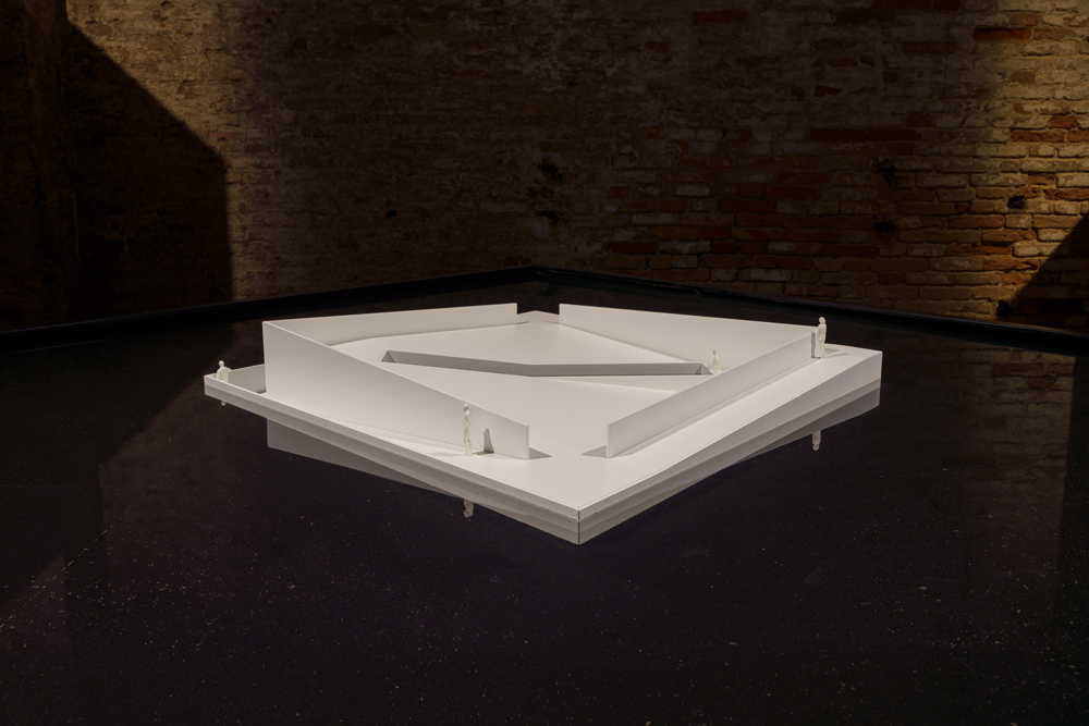Model of white, floating platform housed in brick room.