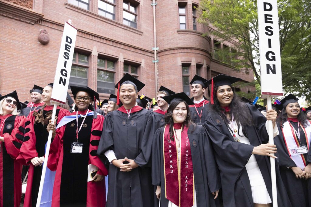 Students gathered for Commencement in caps and gowns holding two design flags
