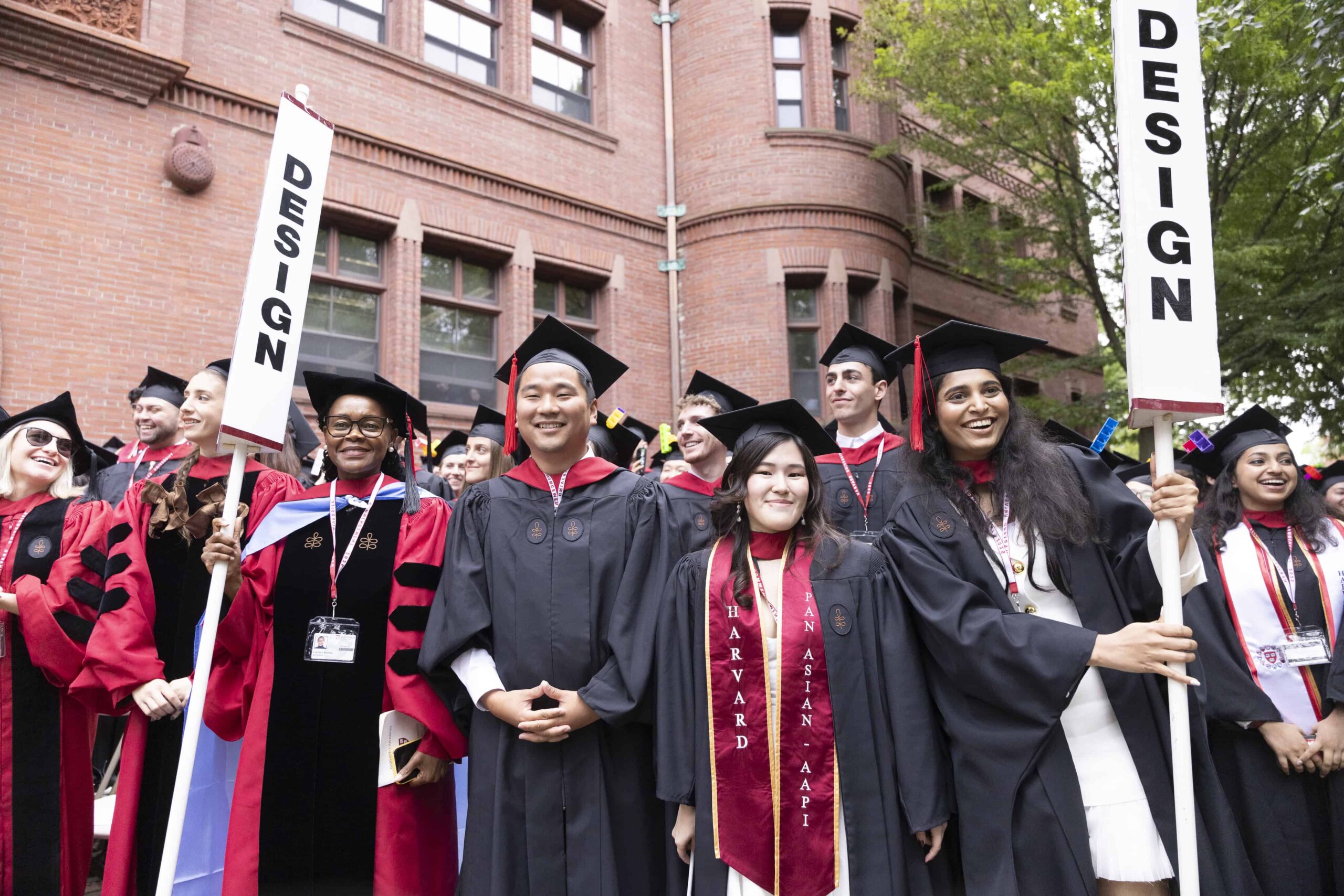 Students gathered for Commencement in caps and gowns holding two design flags