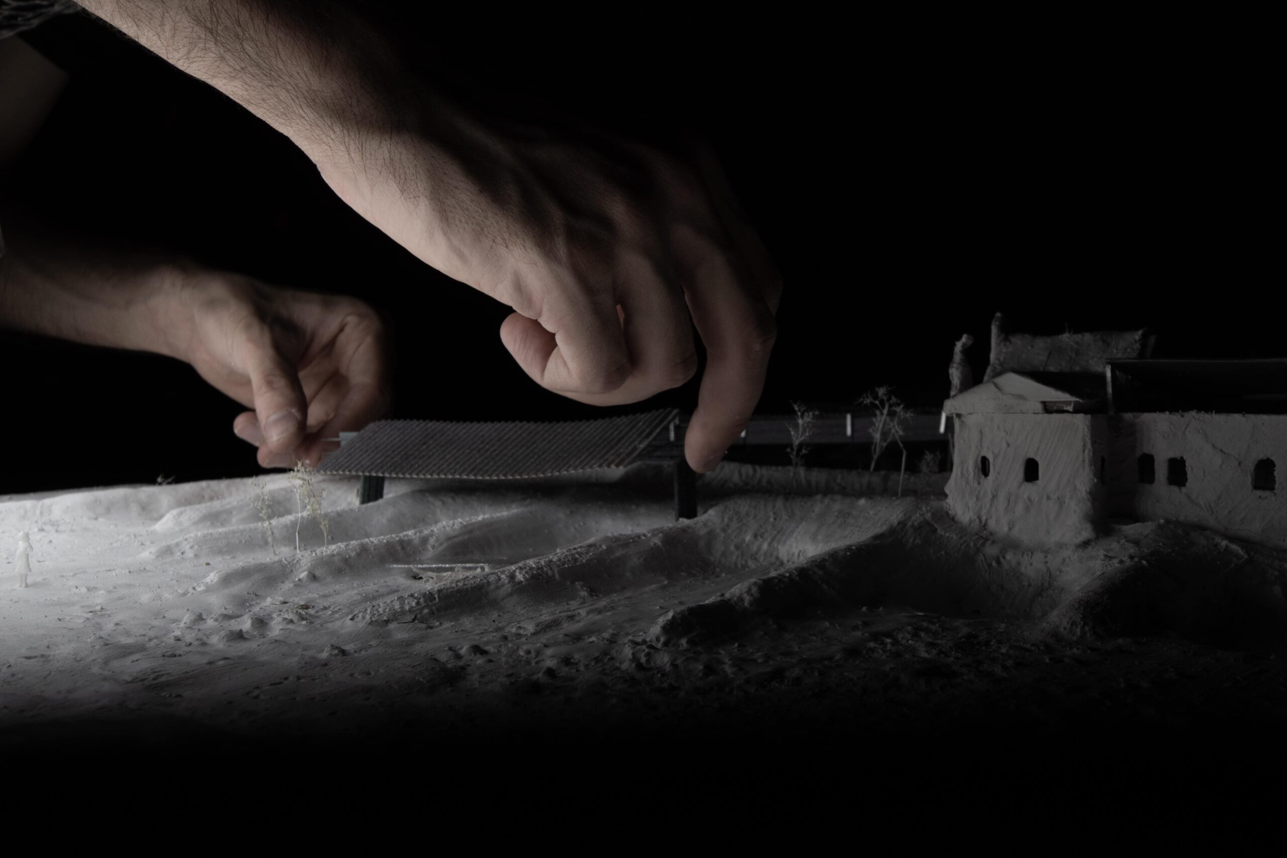 Photo of a model of a building with people's hands moving things around