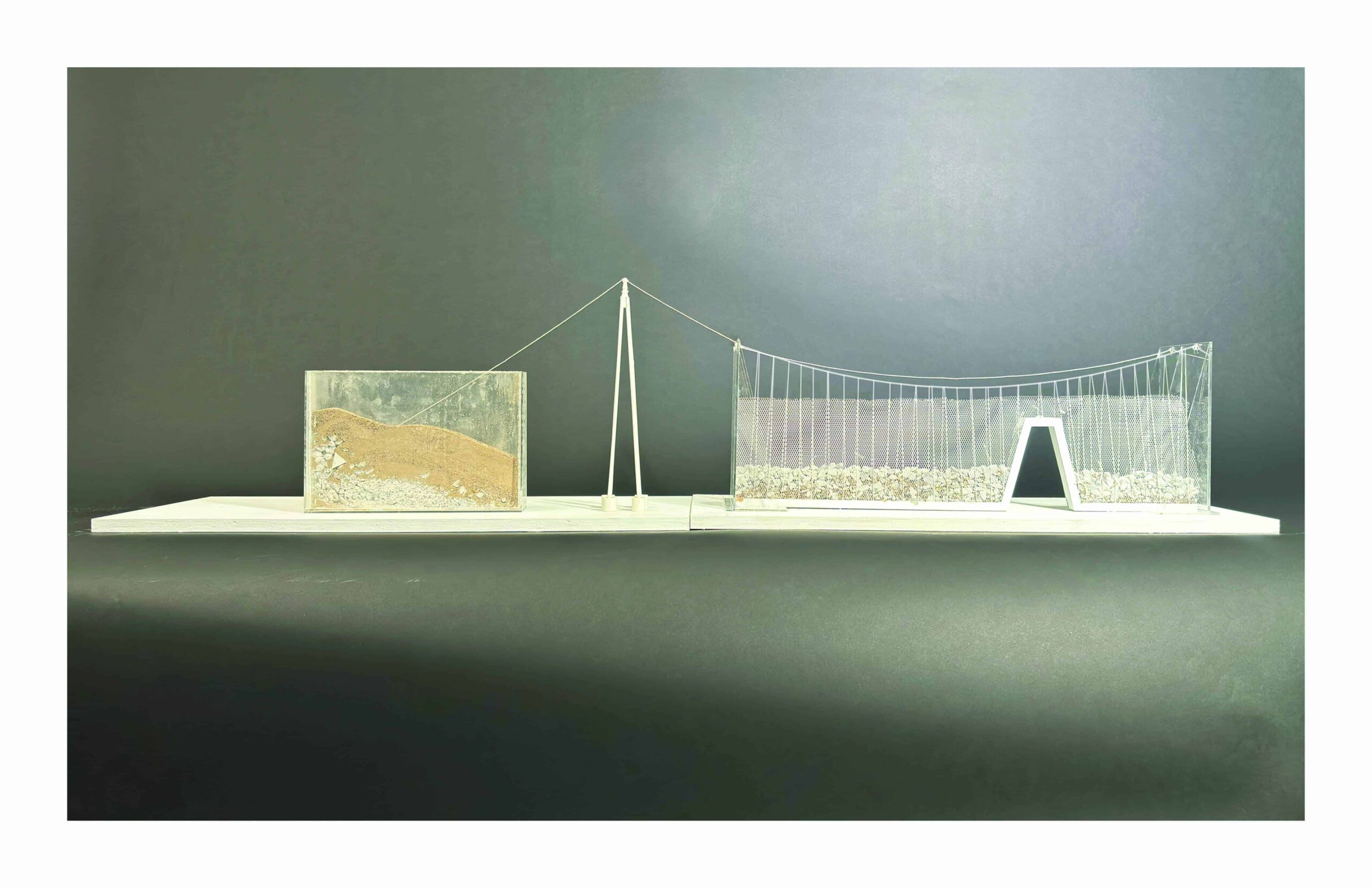 Physical model of a suspension system with sand and gravel enclosed in transparent mesh, supported by a central mast.
