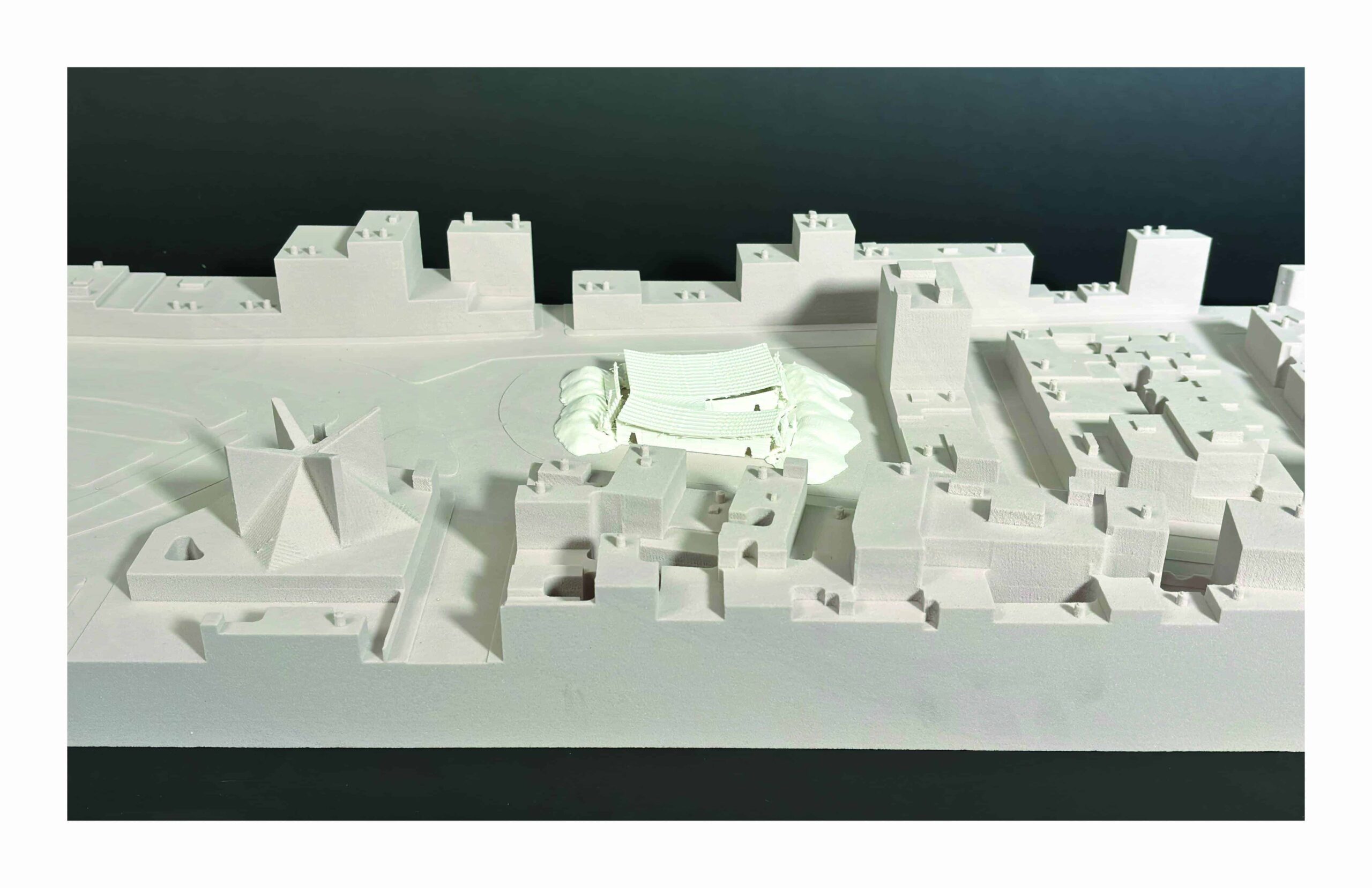 Site model showing a white pavilion-like structure with a canopy and rubble mounds in an urban context.