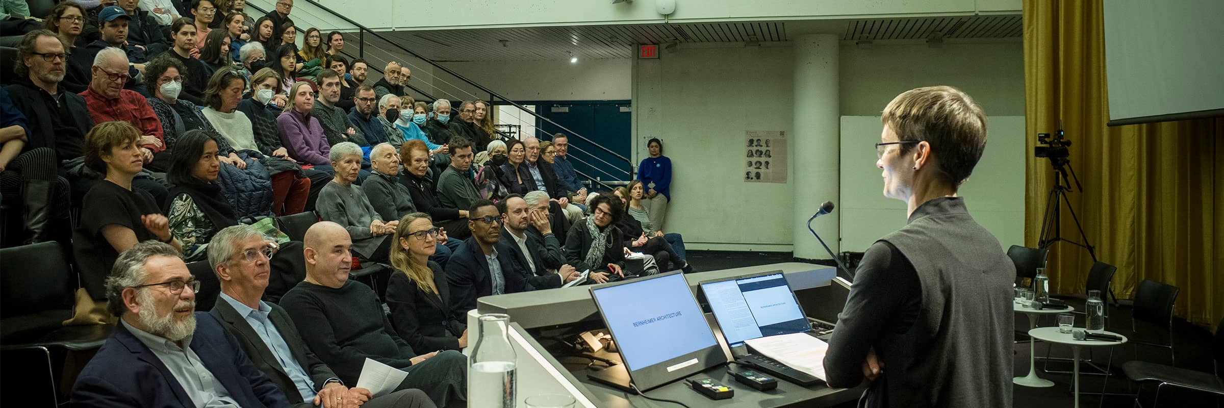 Dean stands at a podium presenting to an auditorium audience.