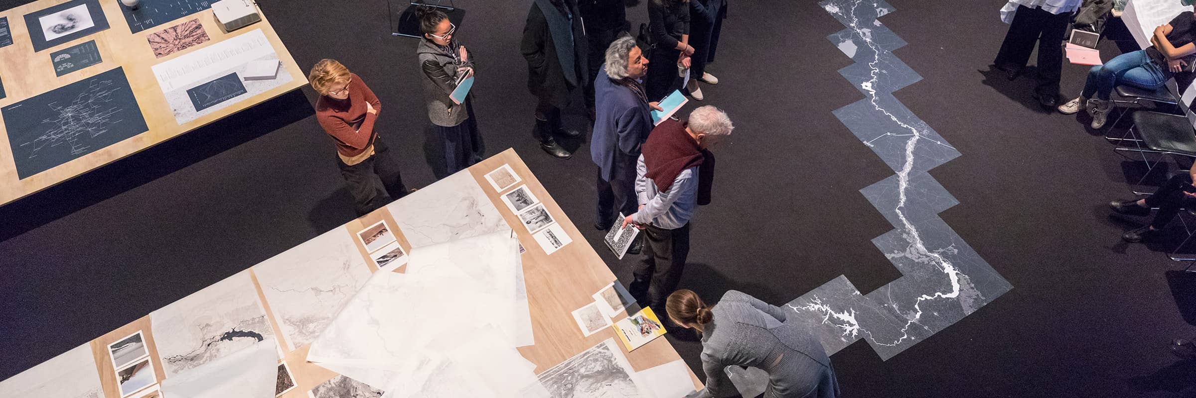 Group of people surrounded by student projects viewed from overhead during a thesis exhibition.