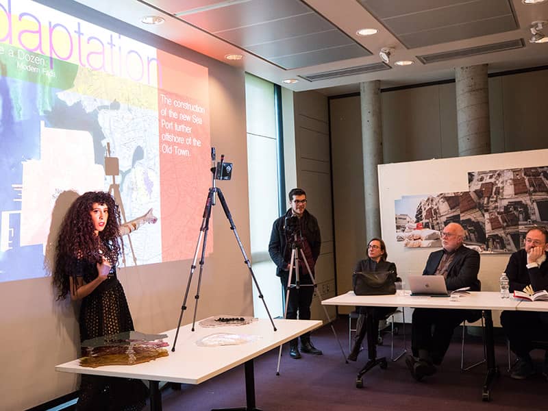 Student standing in front of projector presenting to a panel.