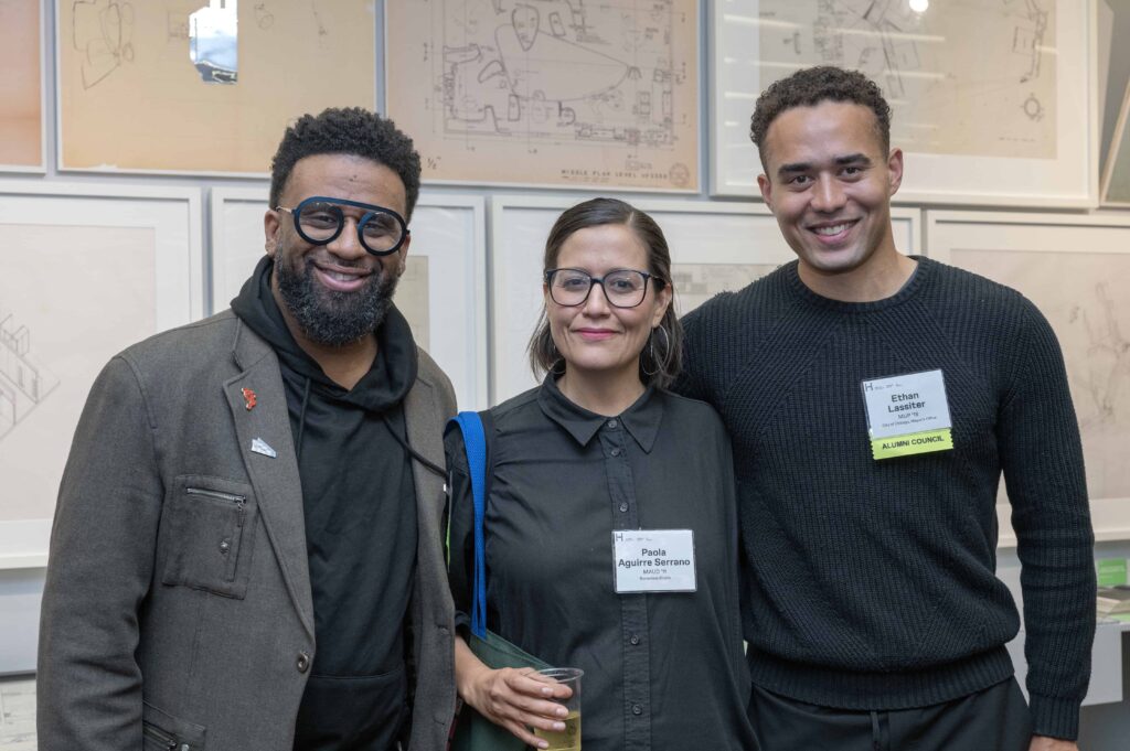 Three alumni standing with a gallery exhibition in the background