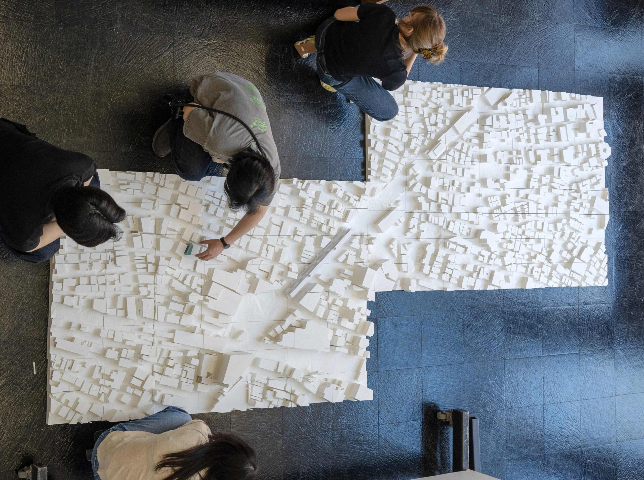 Students crouch around large model of a city.