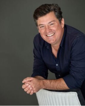 Headshot of Pedro H. Alonzo smiling widely and leaning against a chair with his hands clasped in front of him.