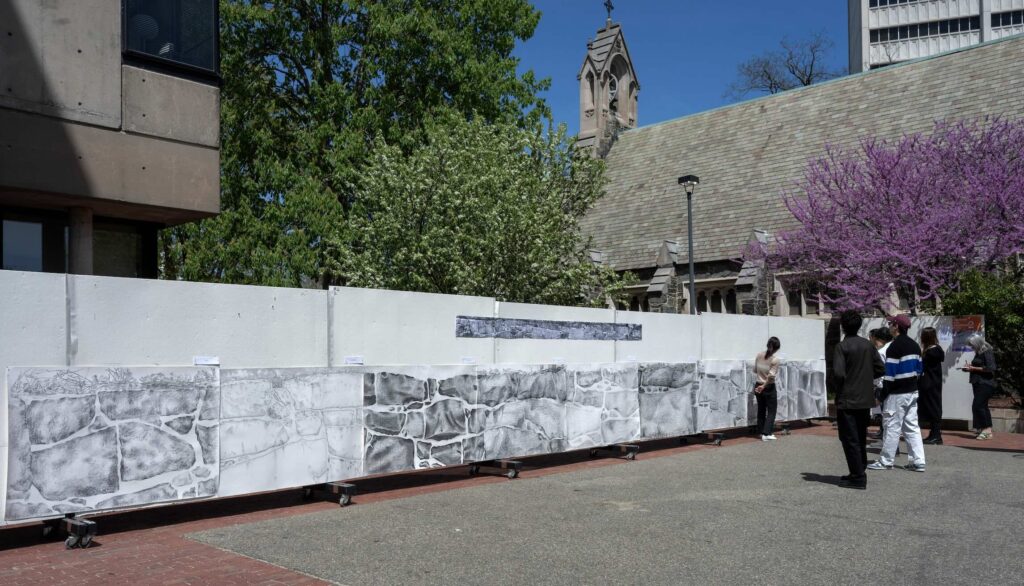 students stand in front of a black and white drawing of a life-size brick wall