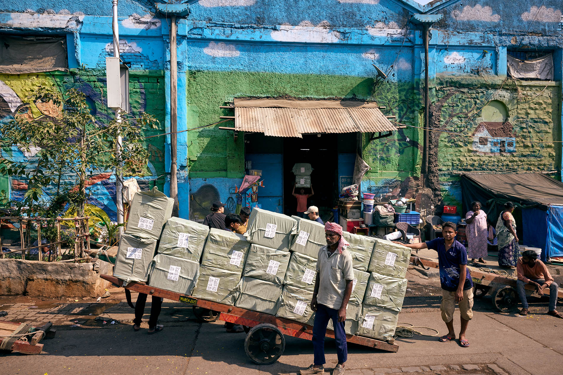 Workers with big cart of packages in front of a blue painted warehouse