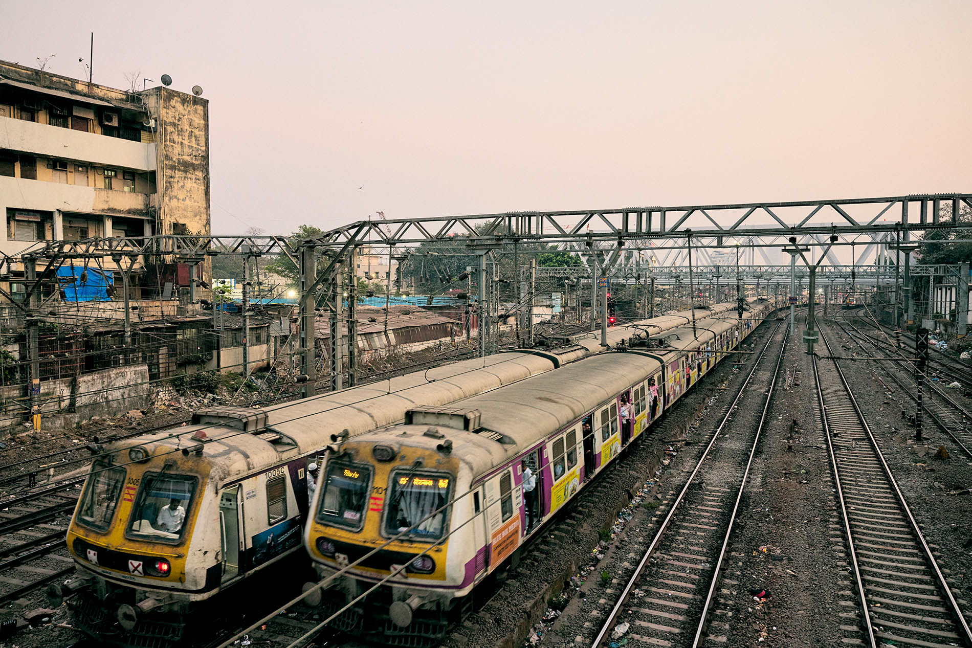 Two trains on train tracks with a dilapidated building to the left