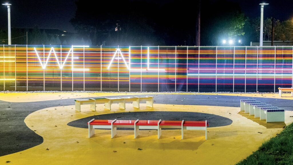 Colorful neon letters spelling out We All on a fence.