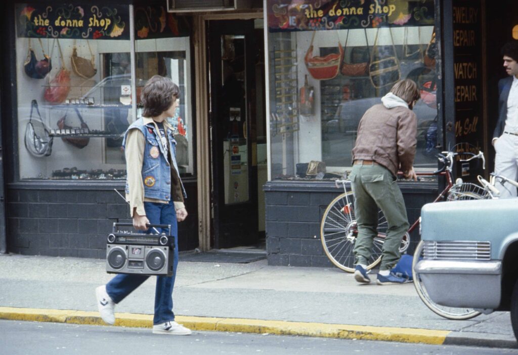 Image of man walking with boom box down New York city street in the 80s.