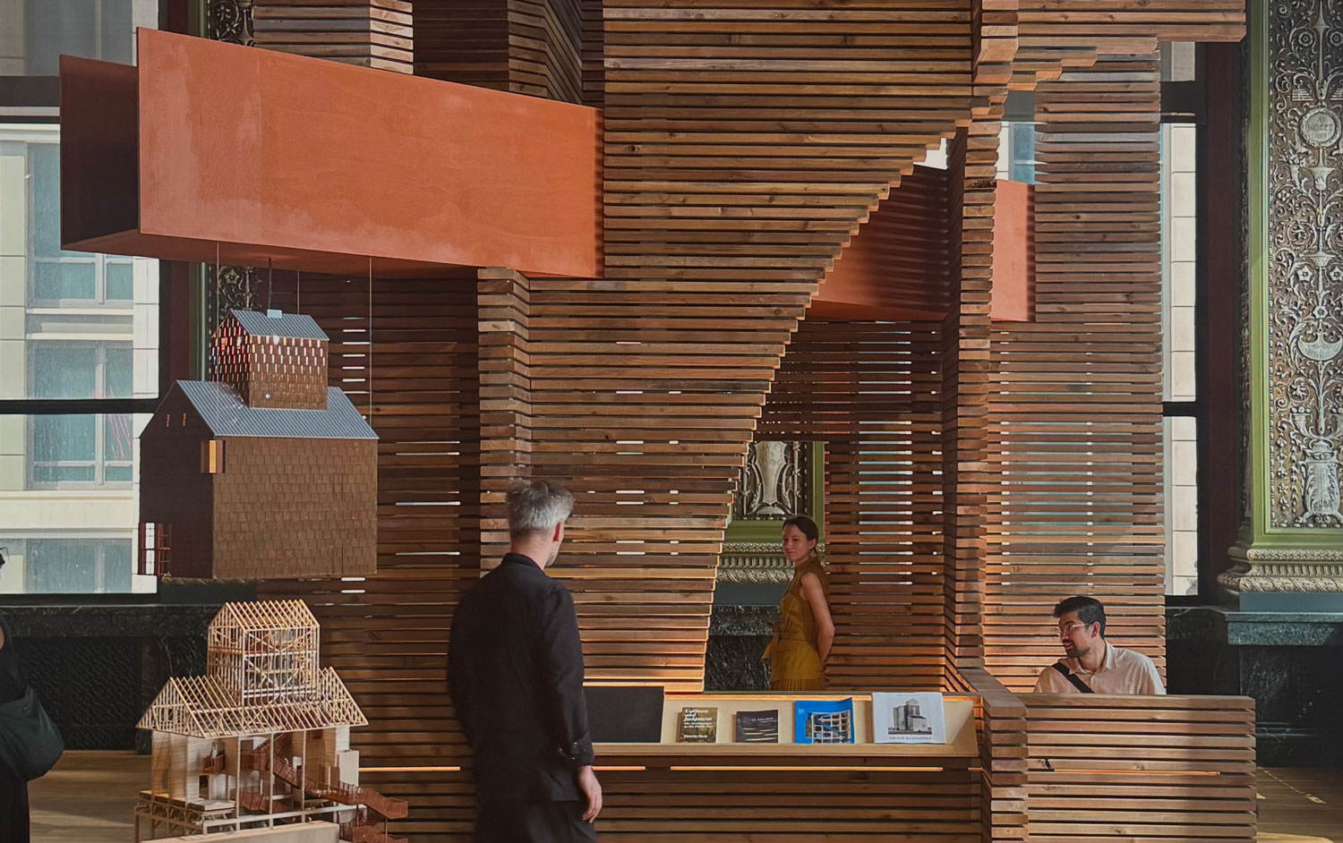 Wooden installation with people and orange beam.
