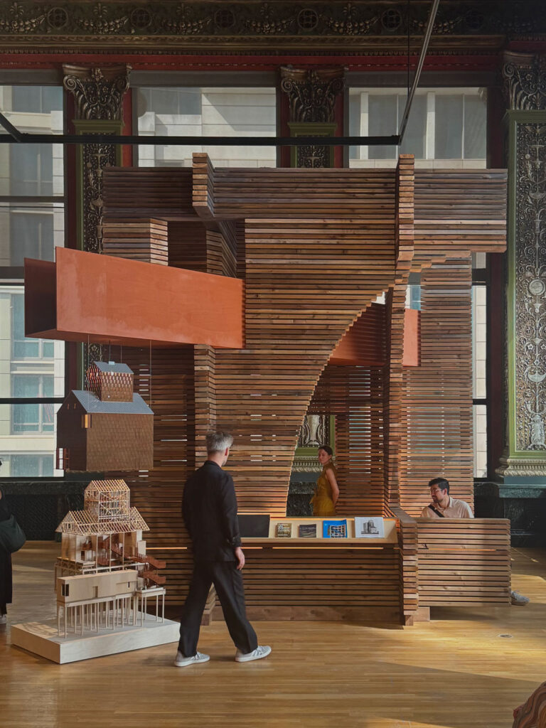 Wooden installation with people walking around it.